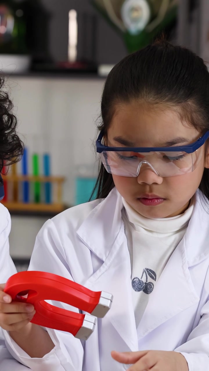 Nuori opiskelija suorittaa fysiikan koetta suojalasit päässään käyttäen punaista hevosenkenkämagneettia.