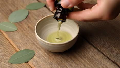 pouring essential oil from a dropper bottle into a bowl with eucalyptus leaves