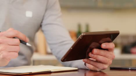 man writing on a diary while using digital tablet in kitchen 4k