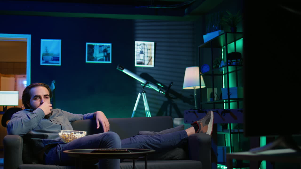 집주인이 집에서 지루해서 간식을 먹고 tv를 보고 있습니다.