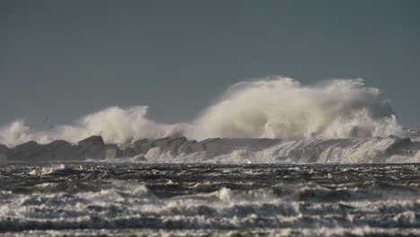 wide shot of giant waves crashing over the breakwater and sending up spray during an extreme storm, slow motion