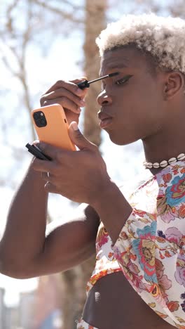 focused black transgender person applying mascara on street