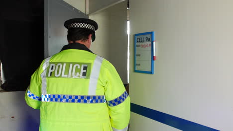 a police officer in a high-visibility jacket escorts a woman prisoner into a prison cell