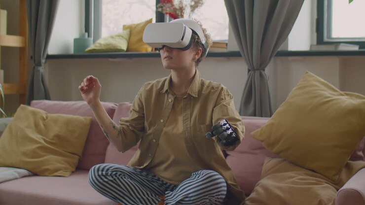 Ragazza con braccio protesico seduta sul divano e che usa un visore VR