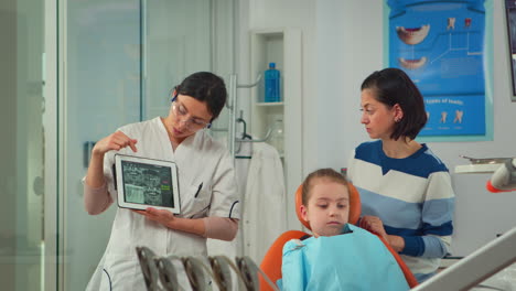 pediatric dentist showing teeth x-ray on tablet pc computer screen to mother