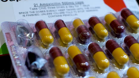 a close-up view of amoxicillin capsules as the dark red and yellow components are delicately arranged into their original packaging, and two pills are taken out