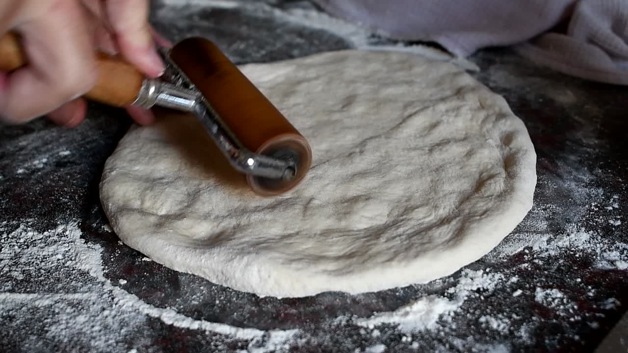 Working on a home made pizza dough with the bare hands on a marble kitchen counter. Side view, medium high angle. Natural window light
