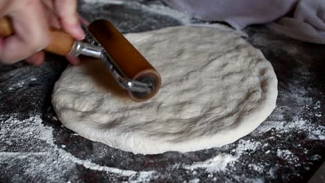 working on a home made pizza dough with the bare hands on a marble kitchen counter. side view, medium high angle. natural window light