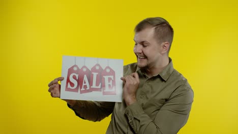 Great-discounts.-Happy-cheerful-blonde-man-in-blue-shirt-showing-Sale-word-advertisement-inscription