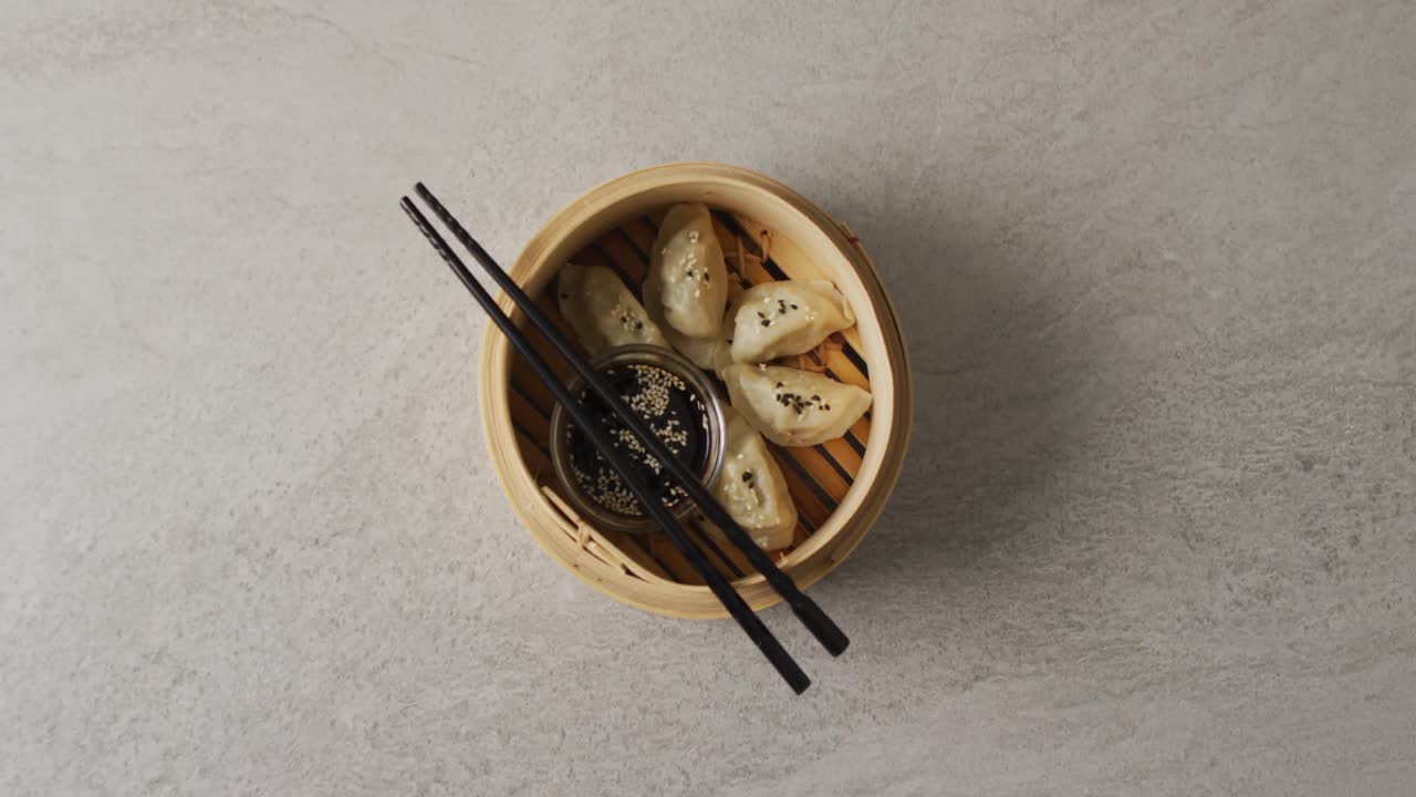 Composizione di una vaporiera di bambù con ravioli gyoza e bacchette con salsa di soia su sfondo grigio
