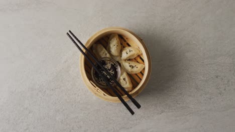 composition of bamboo steamer with gyoza dumplings and chopsticks with soy sauce on grey background