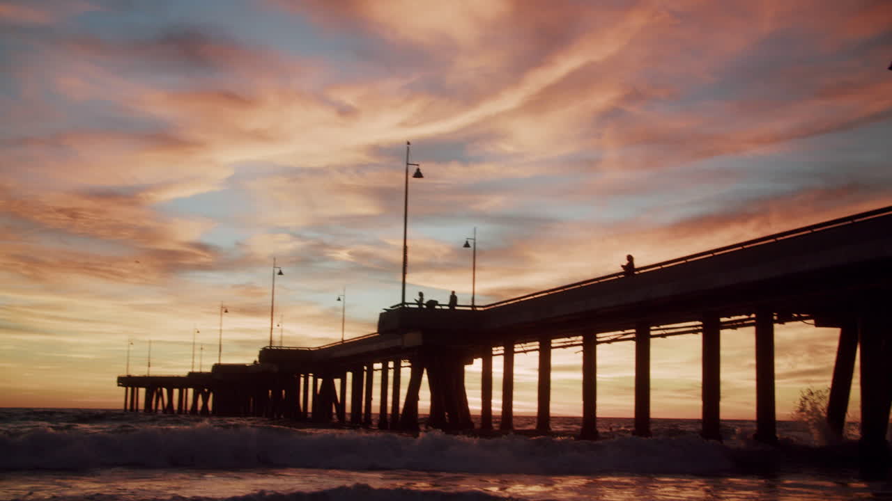 Dramatic sunset over a long pier with silhouetted figures