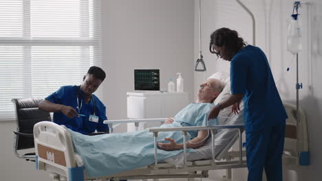 a team of african ethnic group doctors a man and a woman talk to an elderly male patient. a doctor and a nurse talk to a bedridden patient in a hospital ward