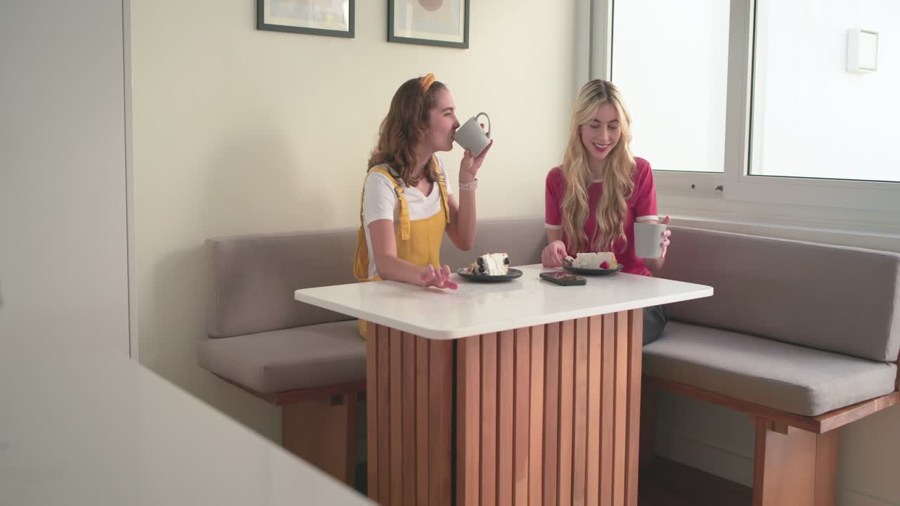 Brindis de café que provoca risas entre amigas levantando tazas y probando pastel en un rincón de desayuno.