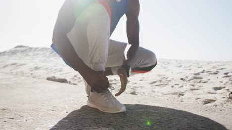 midsection of african american man tying shoelaces during exercise outdoors on beach