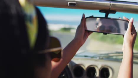 Mujer-Afroamericana-Ajustando-El-Espejo-Retrovisor-Mientras-Está-Sentada-En-El-Auto-Convertible-En-La-Carretera