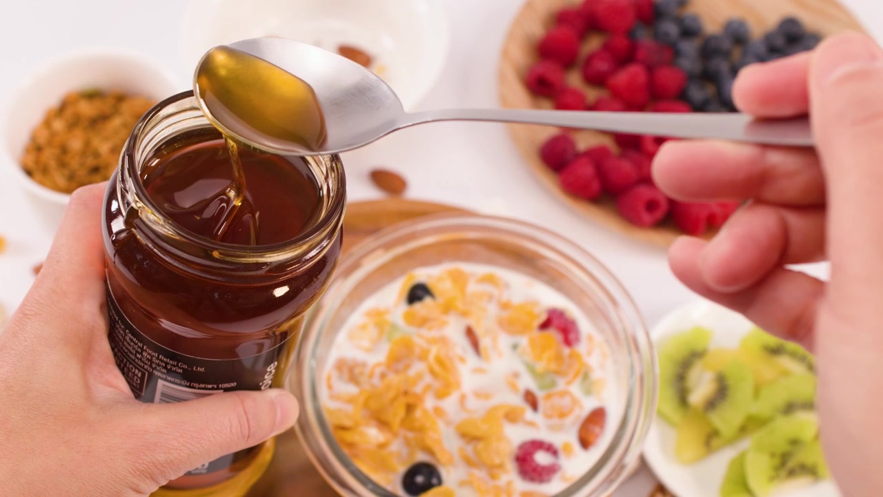 Primo piano dall'alto di miele che viene prelevato con un cucchiaio sopra una ciotola di cereali