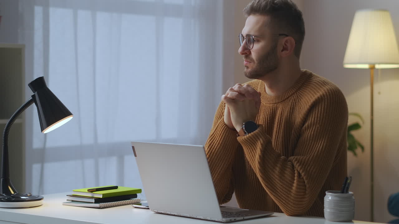 joven está esperando un mensaje importante sentado en la mesa con la computadora portátil abierta mirando la pantalla persona pensativa retrato medio en el apartamento