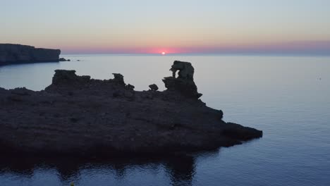 Drohne-Schwenkt-Zurück-über-Eine-Kleine-Abgelegene-Bucht-Entlang-Der-Küste-Menorcas,-Mit-Festgemachten-Booten-Und-In-Der-Ferne-Schwimmenden-Paddelboardern