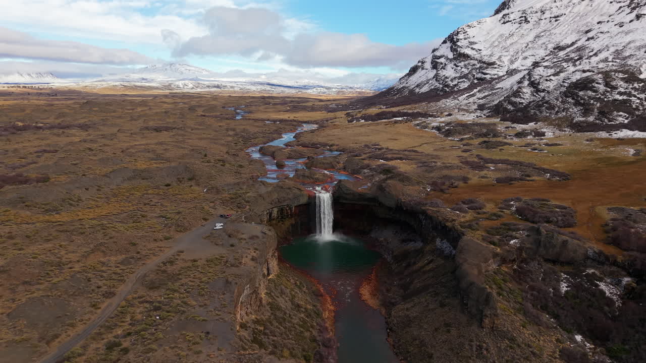 Revealing the unique Salto del Agrio waterfall, with its mineral-stained red rocks and turquoise pool, in a vast Patagonian landscape - A stunning aerial drone shot pulls back and rises