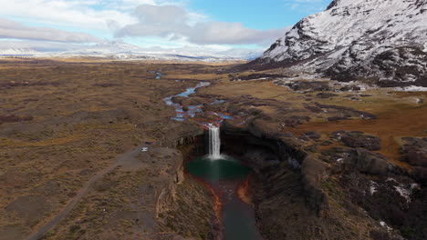 revealing the unique salto del agrio waterfall, with its mineral-stained red rocks and turquoise pool, in a vast patagonian landscape - a stunning aerial drone shot pulls back and rises