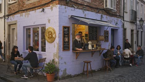 charming purple cafe with bitcoin symbol at the corner, showcasing cozy atmosphere and engaging patrons enjoying drinks and snacks at outdoor tables