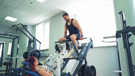 sporty girl doing exercise for legs on a modern simulator in the gym. woman is lifting man by her strong legs on a fitness machine in the light sports center.