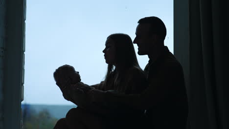 silhouette of a young family with infant baby. mother waves her son and talks to him.