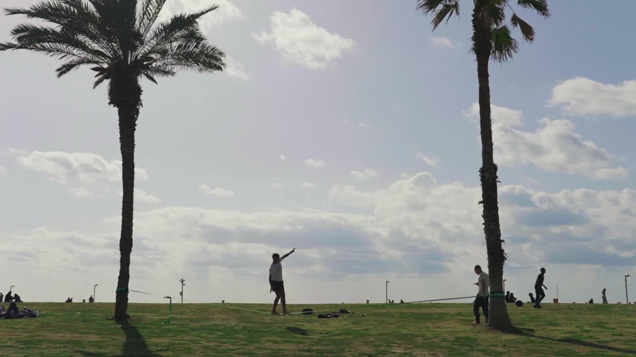 Tel Aviv, İsrail'deki plajda çimenlerin üzerinde slackline ipinde yürüyen genç adam.