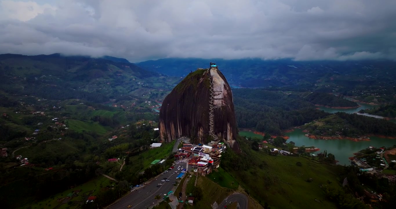Monólito escuro e maciço com escadaria sob céu nublado perto de um lago em Guatapé, Colômbia. Recuo aéreo