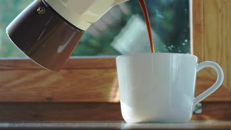 persona vertiendo café caliente en una taza blanca de una cafetera moka