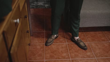 man in green pants and brown loafers standing on a tiled floor, preparing for an event