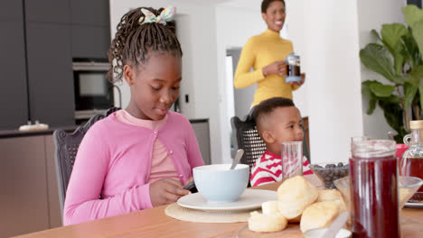 African-american-boy-eating-and-girl-using-smatphone-in-kitchen,-slow-motion