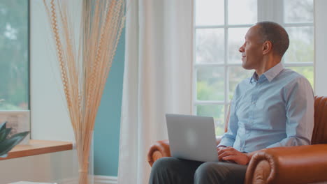 Mature-Man-Or-Businessman-Working-From-Home-Sitting-In-Armchair-Using-Laptop-Computer