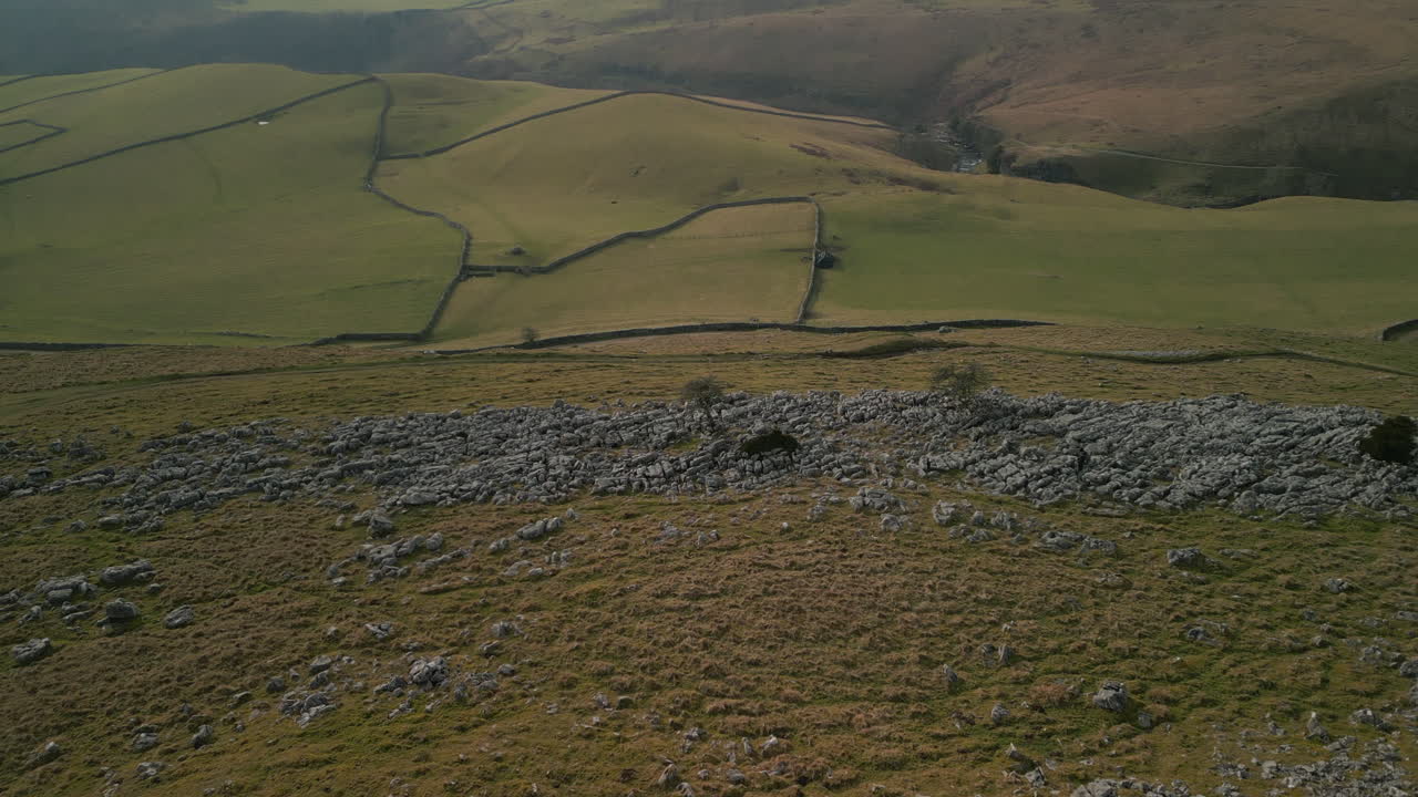 tire de la ladera rocosa revelando campos de retazos verdes en la campiña inglesa en ingleton, yorkshire, reino unido