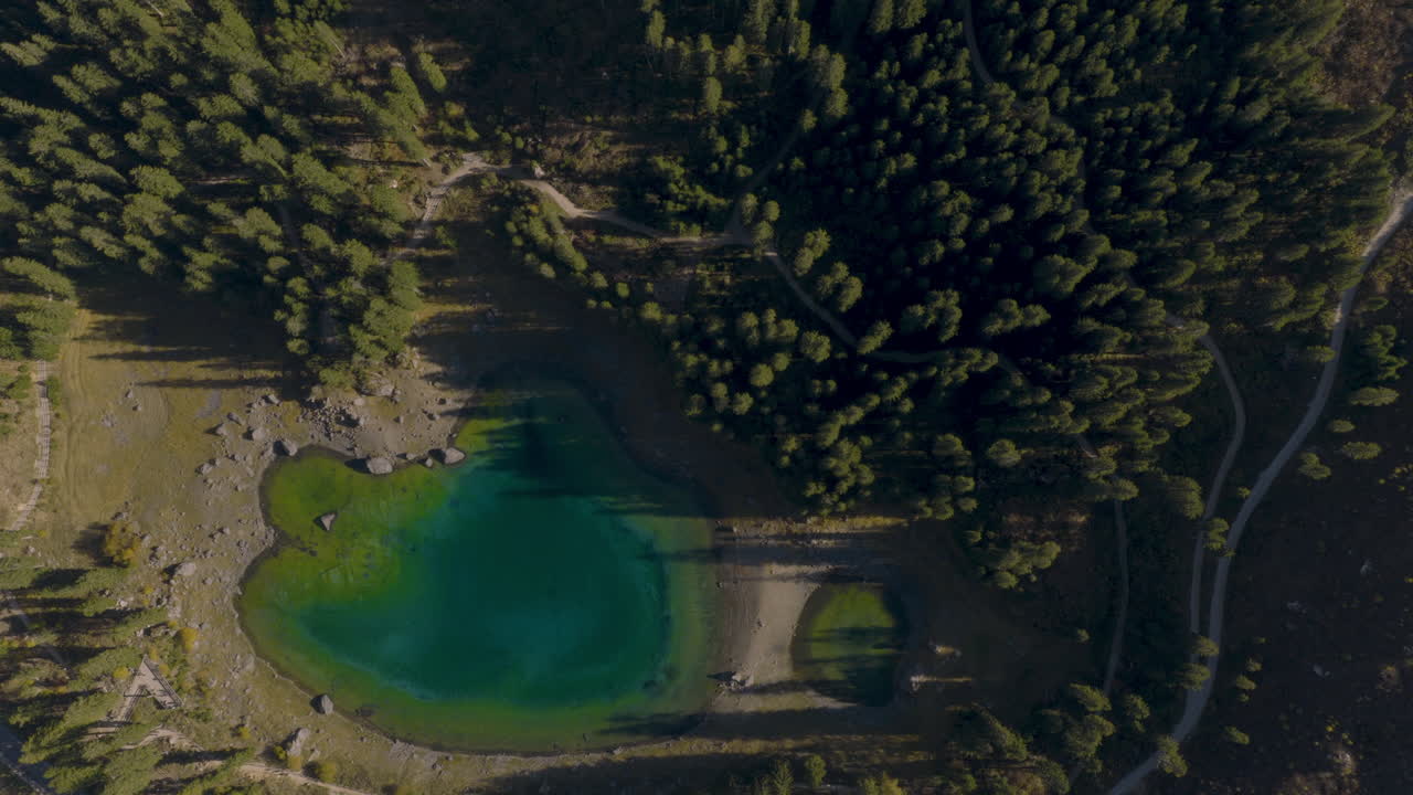 Cinematic aerial view of emerald alpine lake surrounded by forest, rocky shoreline and mountain landscape in the Dolomites, Italy tranquil nature scenery from drone