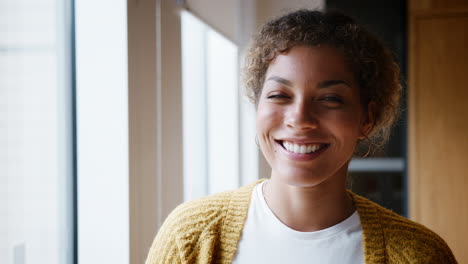 young mixed race millennial woman standing by the window in an office turns to camera and smiles, head and shoulders, close up
