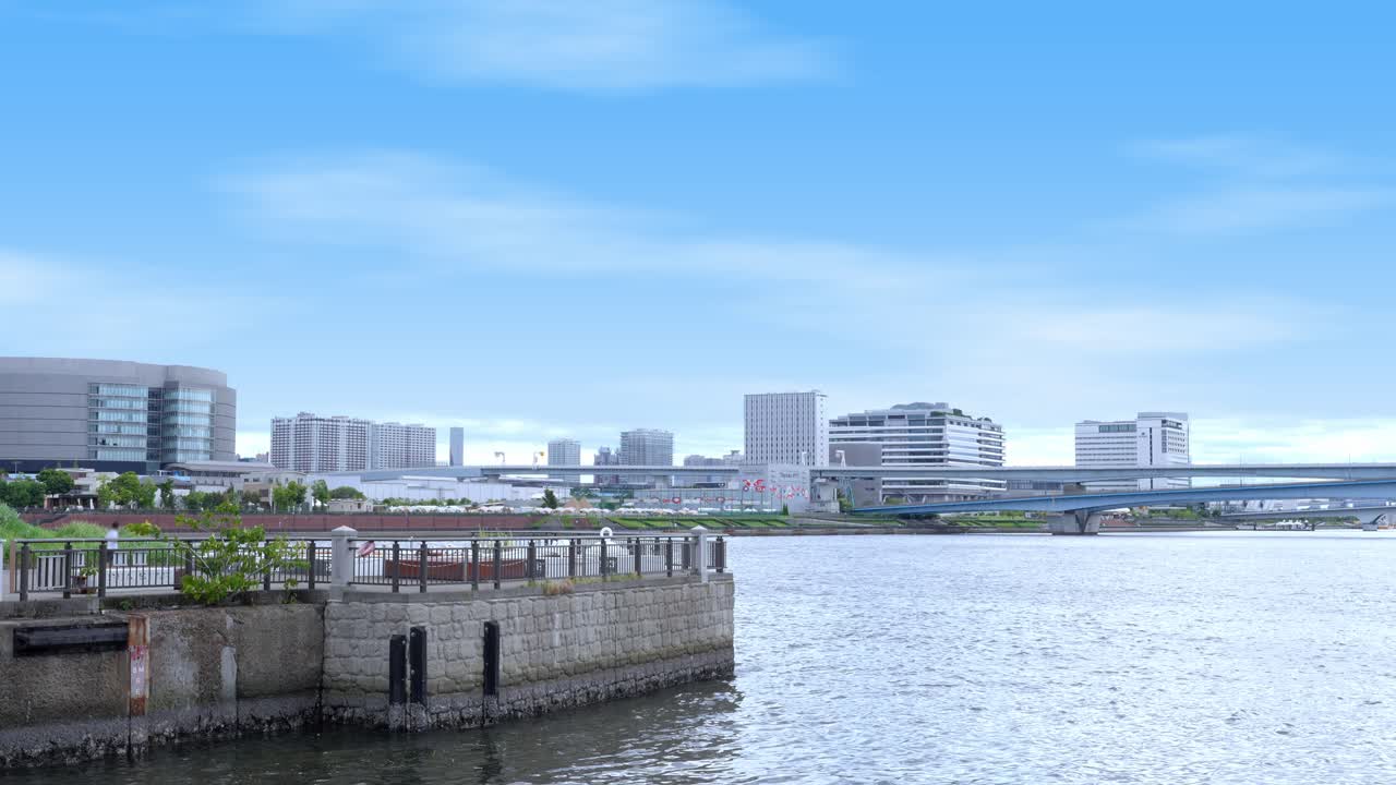 A peaceful wide shot of the Tokyo waterfront with modern buildings, a pier, and the skyline in the distance