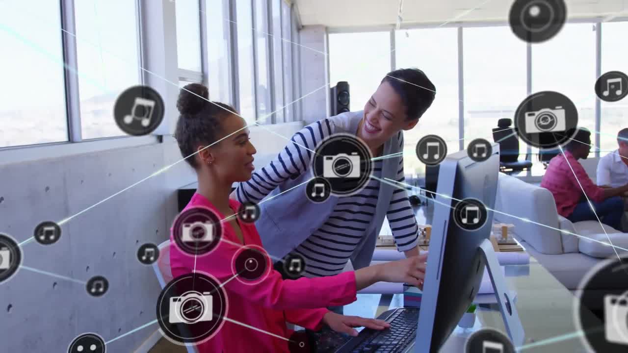 Animation of network of digital icons over two diverse women laughing while discussing at office