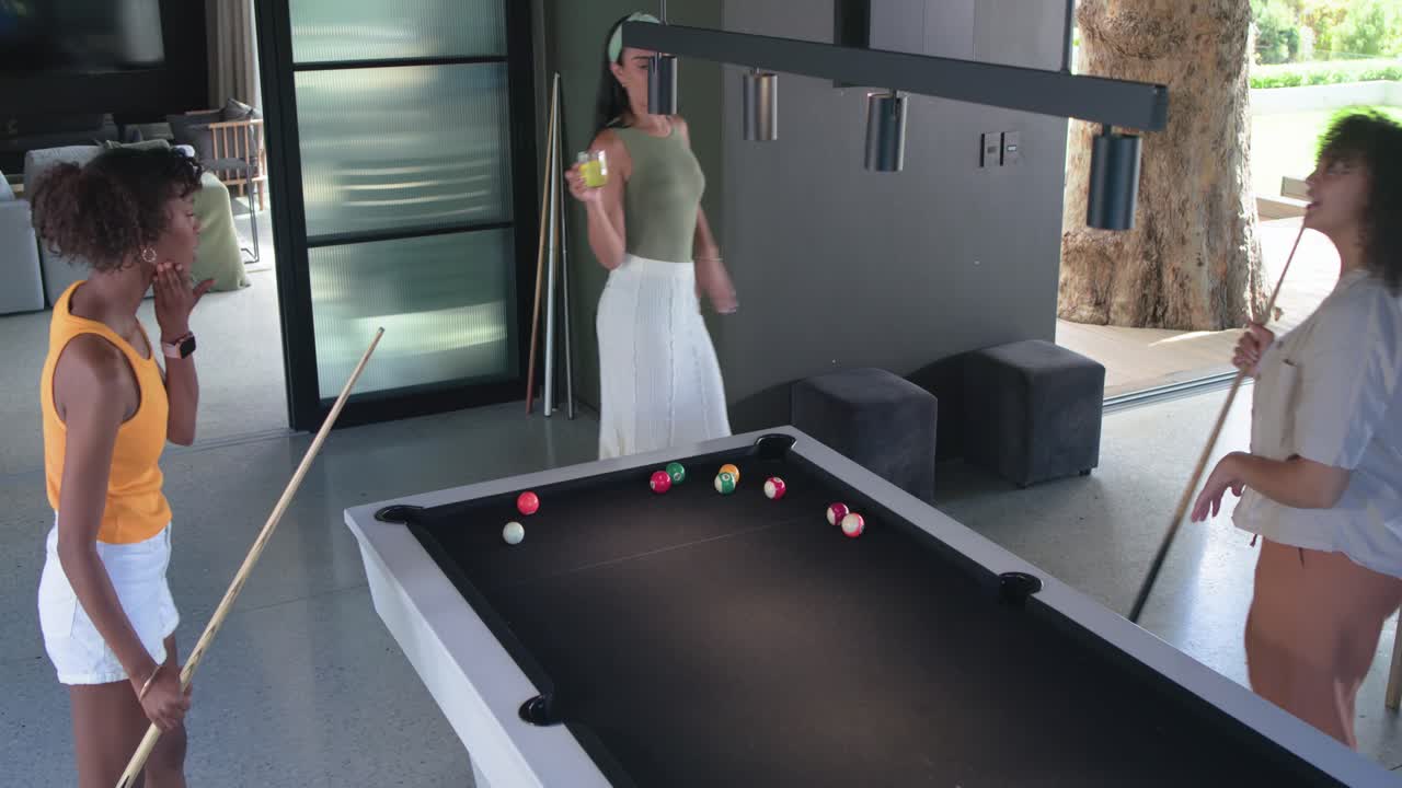 African American female friends tapping cue, taking turns shooting on black-felt pool table for fun