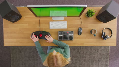 overhead view of female video editor working at computer with green screen in creative office