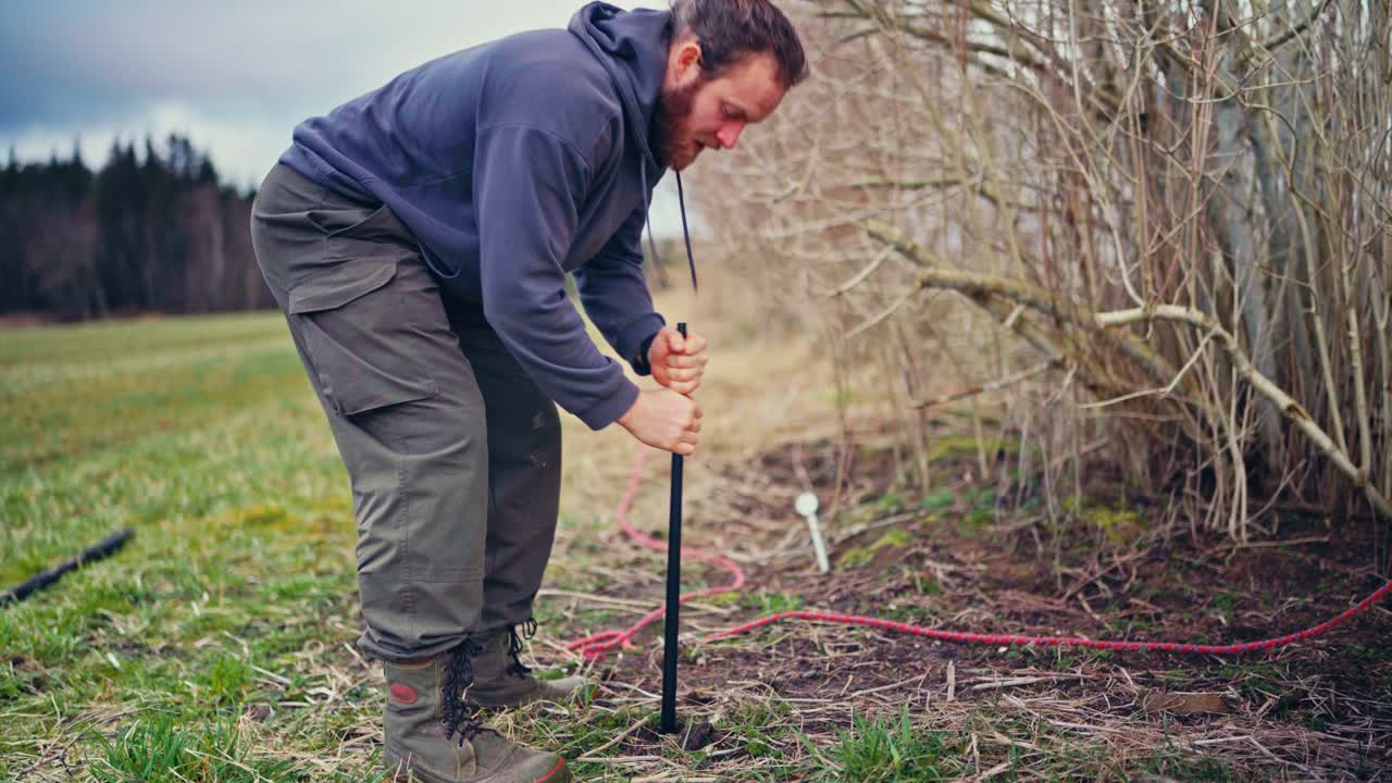 Man Drills Hole For Wooden Post While Constructing Fence - Wide Shot