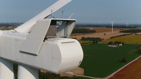 wind farm with close up of nacelle for inspection using a drone orbiting around the machine against farmland fields in the background