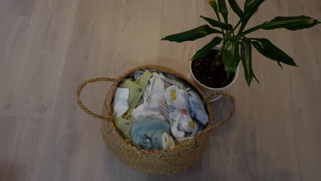 wicker basket filled with folded baby clothes placed on wooden floor, overhead view