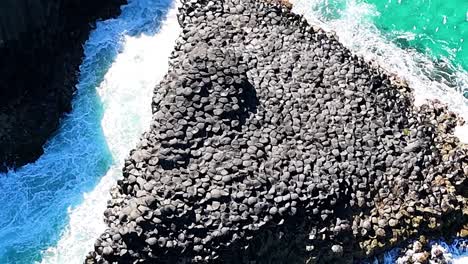close-up aerial view of hexagonal basalt columns meeting turquoise ocean waves.