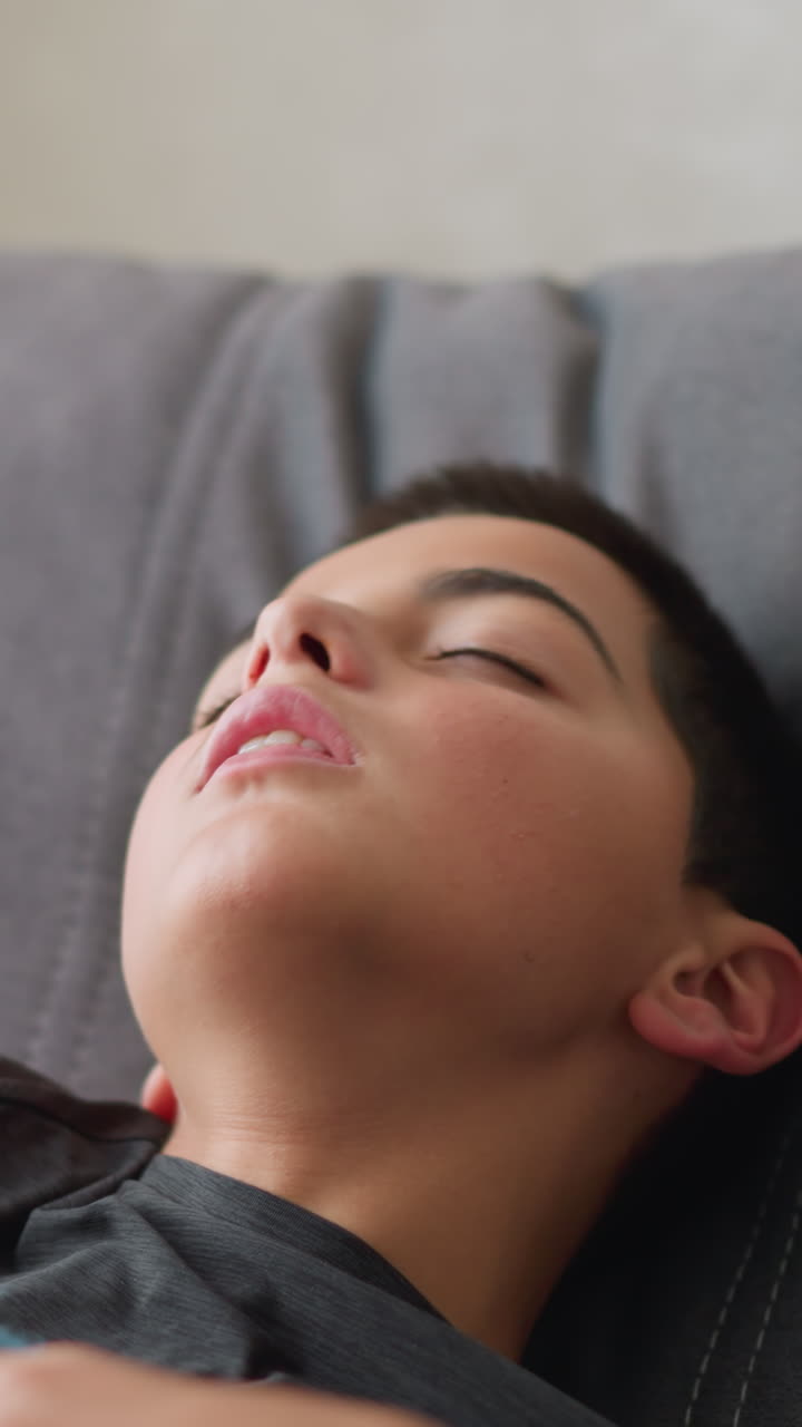 Close-up of child taking nap, adjusting himself for comfort while wrapped in blanket, peaceful indoor setting with soft natural light coming through window, showing restful moment