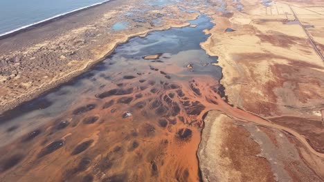 aerial top-down view of the þjórsá river in iceland, where mineral-rich waters create striking orange and black patterns. the braided river flows through vast coastal plains towards the ocean.