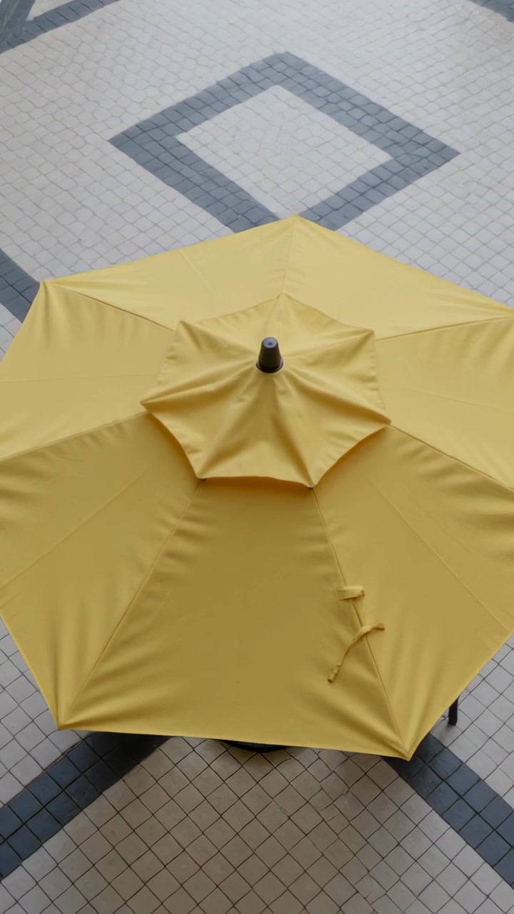 Video verticale: La telecamera si sposta verso il basso rivelando un ombrellone giallo sopra piastrelle a diamante bagnate e una piscina.