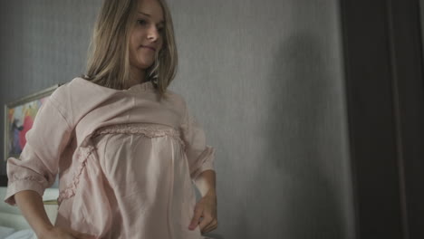 woman trying on a light pink dress in a bedroom