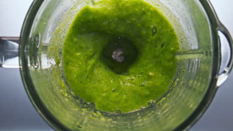 top view green smoothie swirling in blender bowl close up. organic veggies herbs